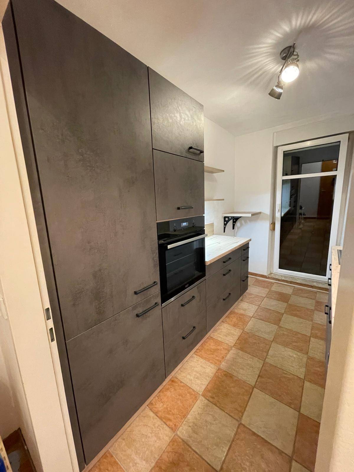 Moderne Küche mit dunklen Schränken, integriertem Backofen und gefliestem Boden.