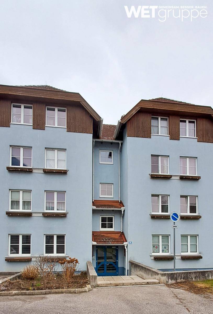 Vorderansicht eines gepflegten Mehrfamilienhauses mit hellblauer Fassade und Holzelementen am Dach.