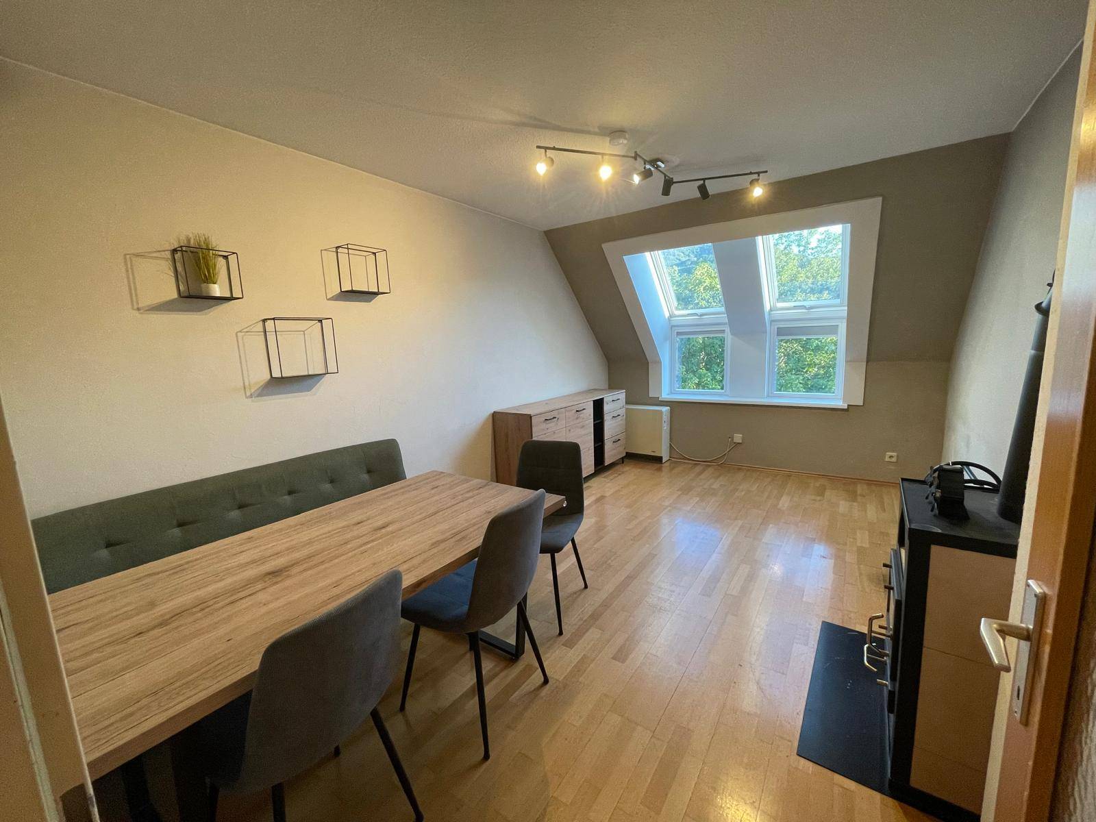 Heller Wohn-Essbereich mit Holzboden, Esstisch, Kaminofen und Dachschrägenfenster.