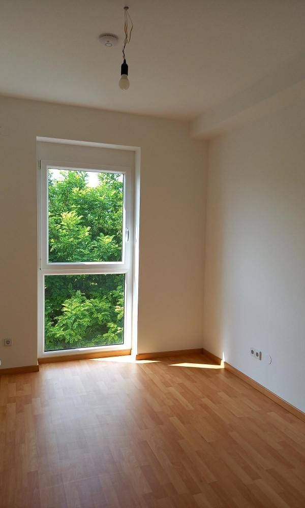 Helles Schlafzimmer mit Holzboden und großem Fenster, das eine angenehme Atmosphäre schafft.