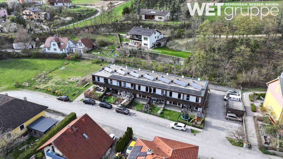 Übersicht einer Reihenhaussiedlung mit Solaranlagen auf den Dächern und angrenzenden Gärten.