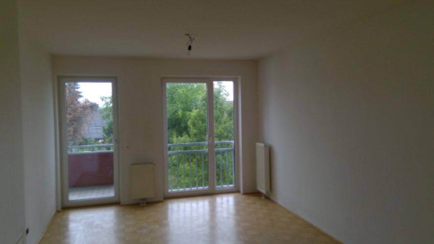 Heller Raum mit Laminatboden und zwei großen Fenstern, die Zugang zum Balkon bieten.