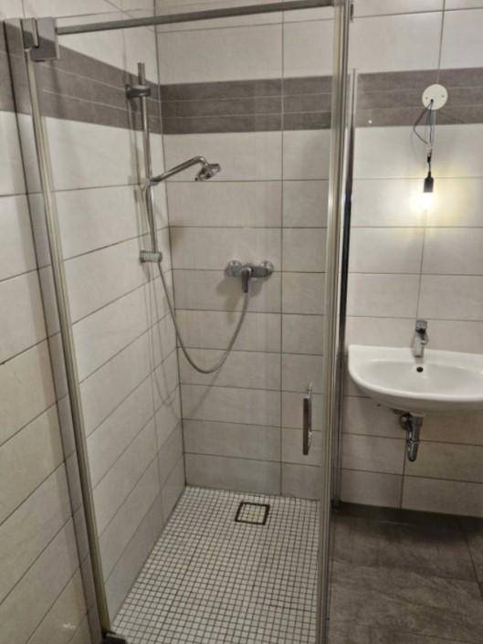 Modernes Badezimmer mit Duschkabine, weißen und grauen Fliesen sowie einem Waschbecken.