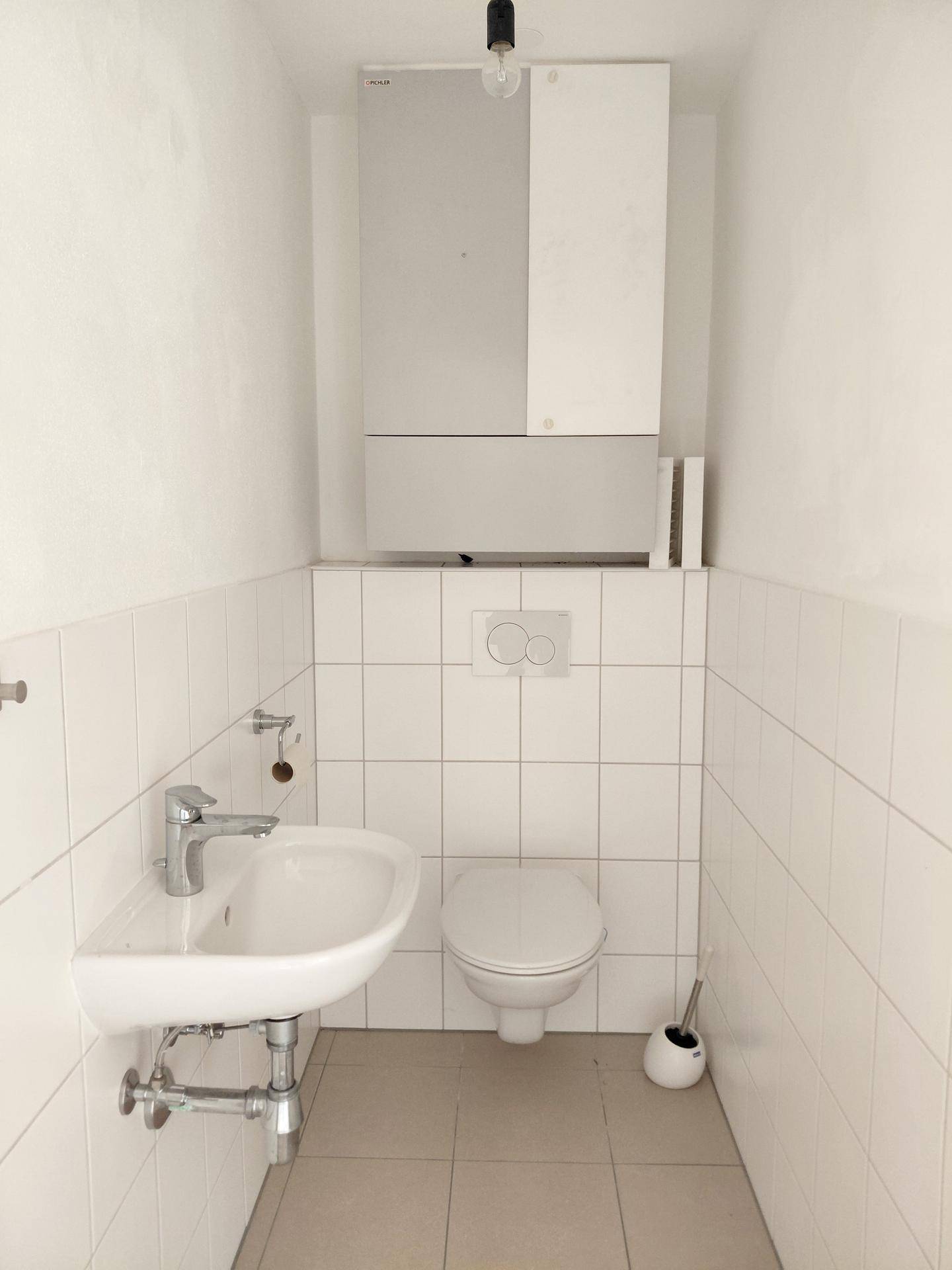 Kleines Gäste-WC mit Wand-WC, Waschbecken und Heizungsanlage, funktional und sauber gefliest.