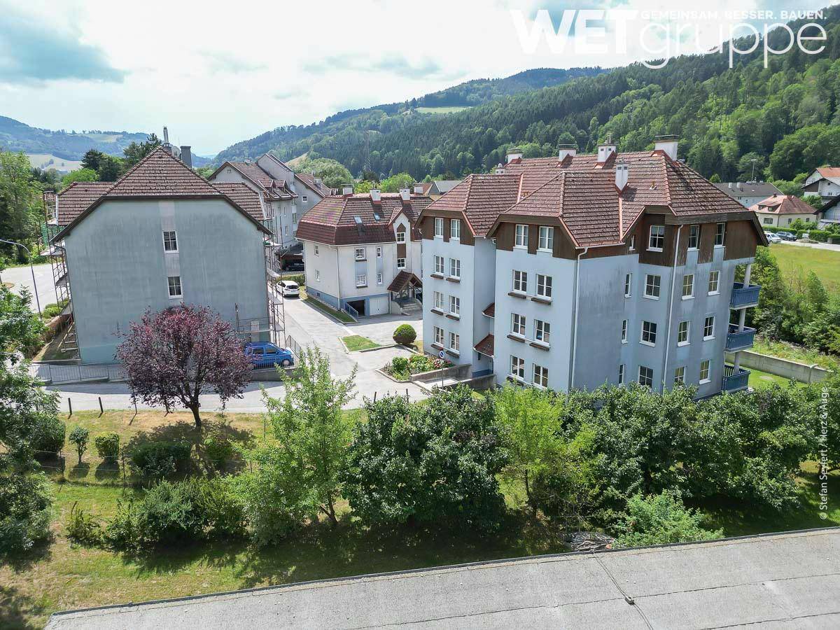Wohngebäude in ländlicher Umgebung, umgeben von Bäumen und Grünflächen, mit Blick auf die Hügel.