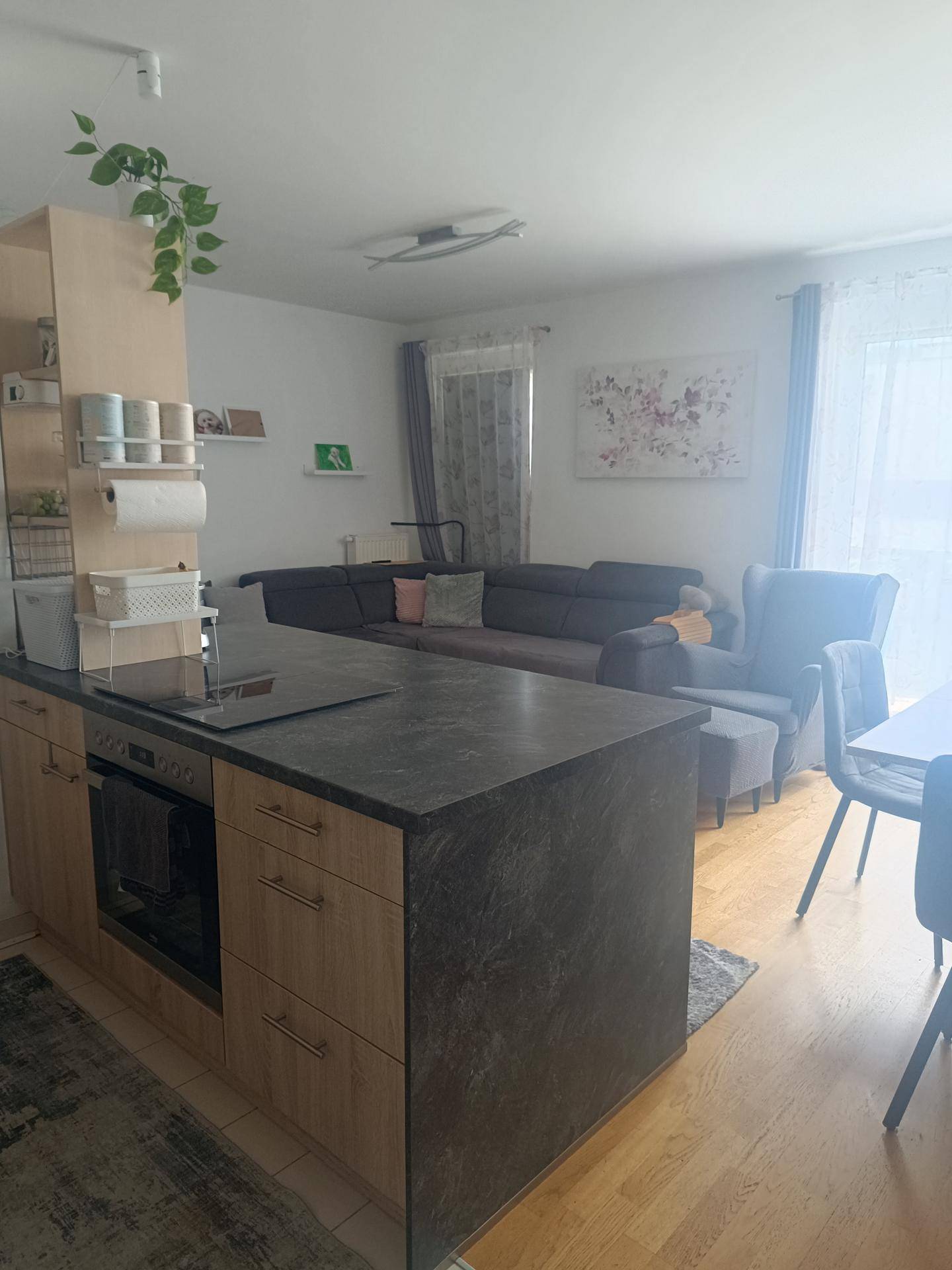 Integrierte Küchenzeile mit dunkler Arbeitsplatte und Blick auf den modernen Wohnbereich mit Sofa.