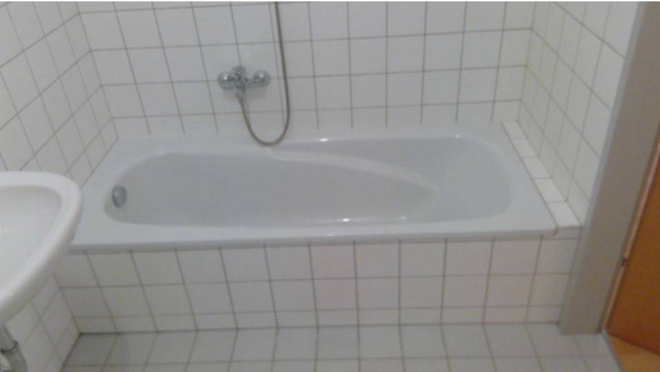 Badezimmer mit weiß gefliesten Wänden und einer integrierten Badewanne mit Duscharmatur.