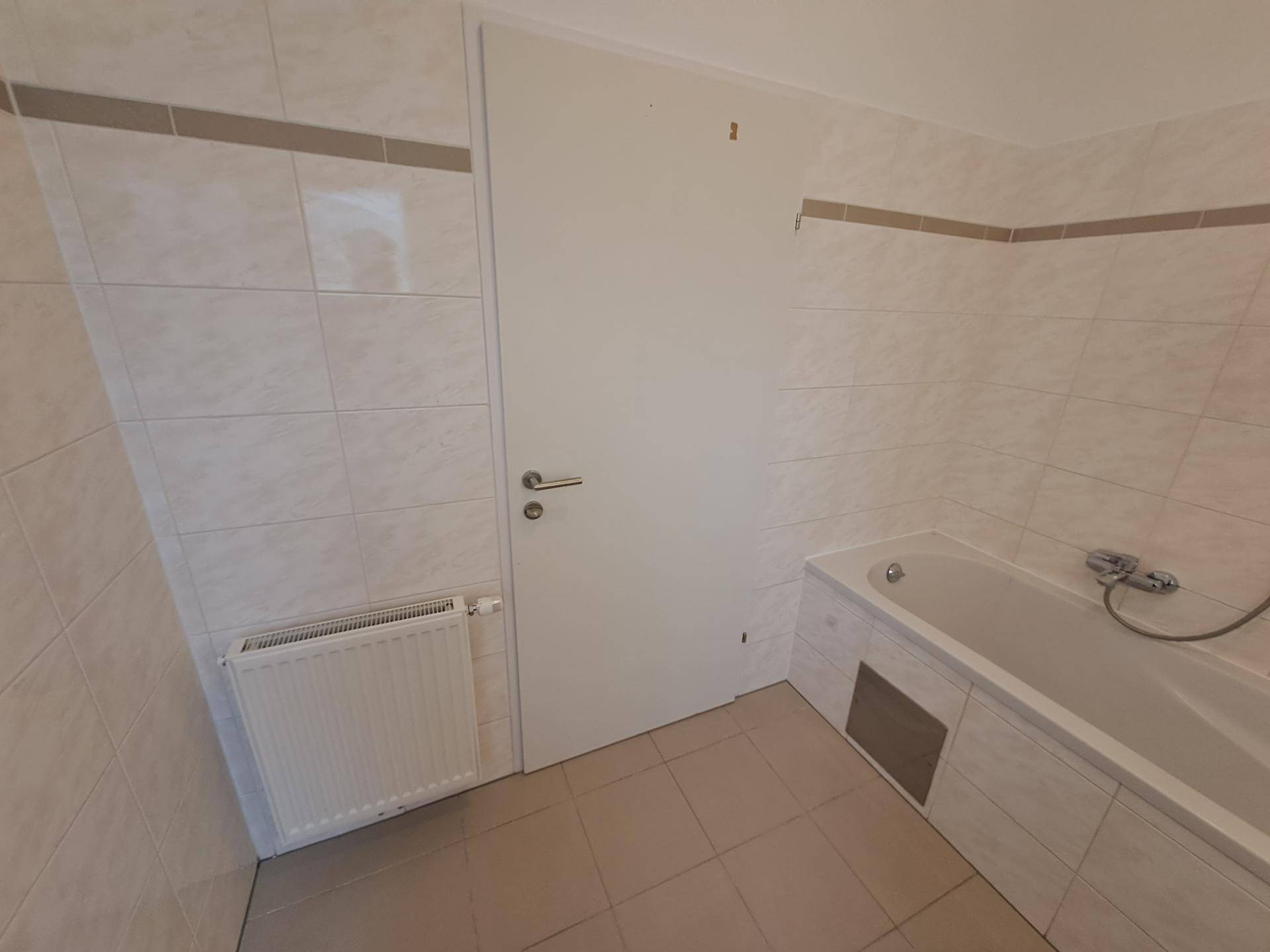 Badezimmer mit weißen Fliesen, einer eingebauten Badewanne und einem Heizkörper.