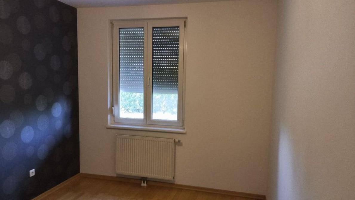Schlafzimmer mit dunkler Akzentwand, Holzboden und Fenster mit Rollläden.