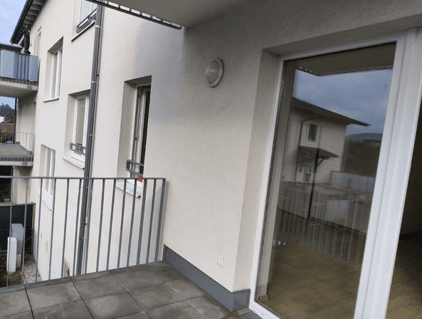 Geräumiger Balkon mit Fliesenboden und Metallgeländer, angrenzend an eine helle Gebäudefassade.