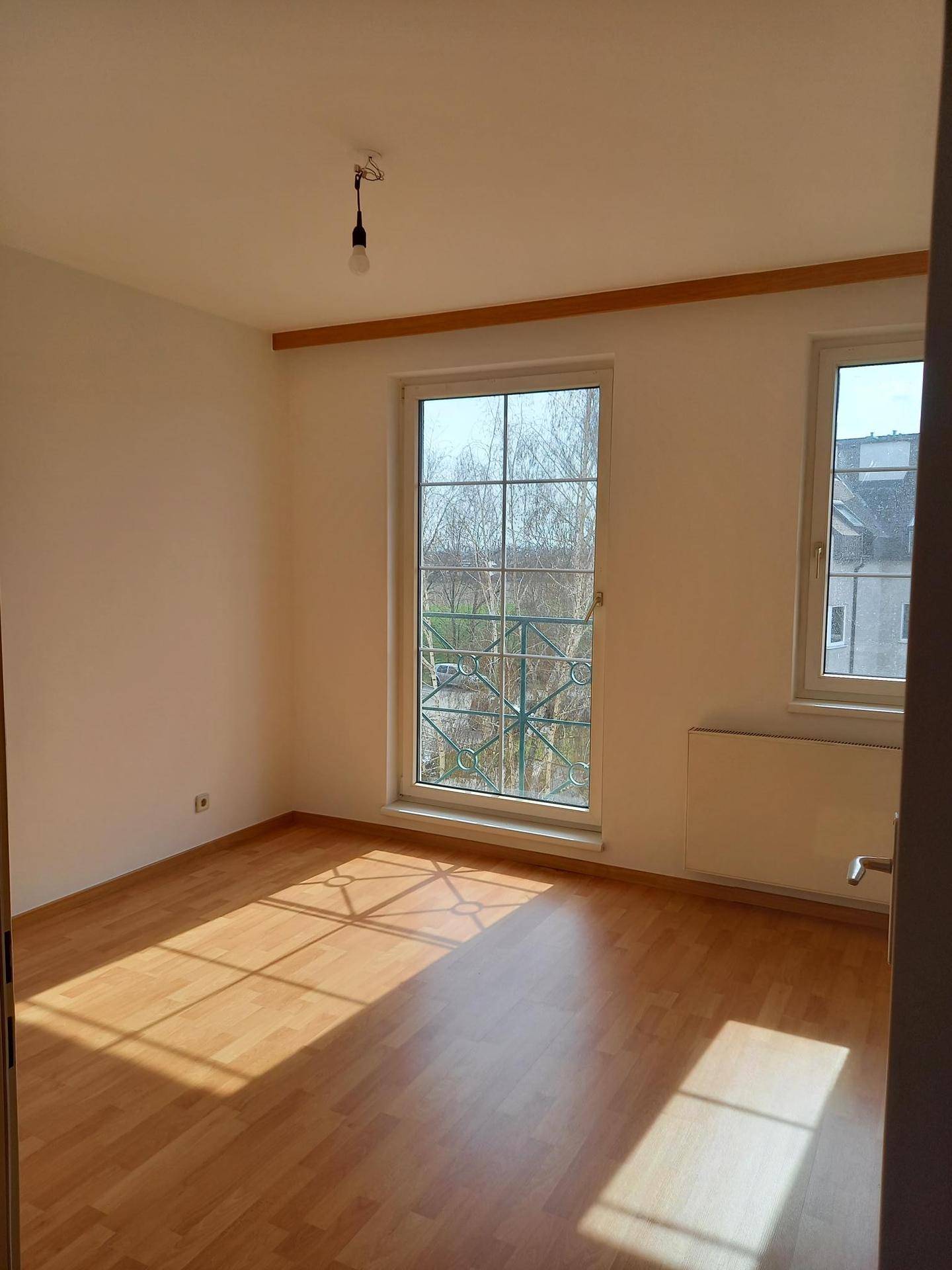 Helles Zimmer mit Laminatboden und einem großen Fenster, das viel Sonnenlicht hereinlässt.