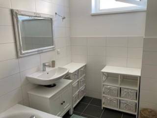 Helles Badezimmer mit modernem Waschbecken, Spiegel und weißen Wandfliesen.