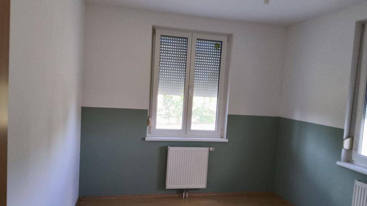 Unmöbliertes Zimmer mit zweifarbigen Wänden, Fenster und Heizkörper, ideal als Schlafzimmer.