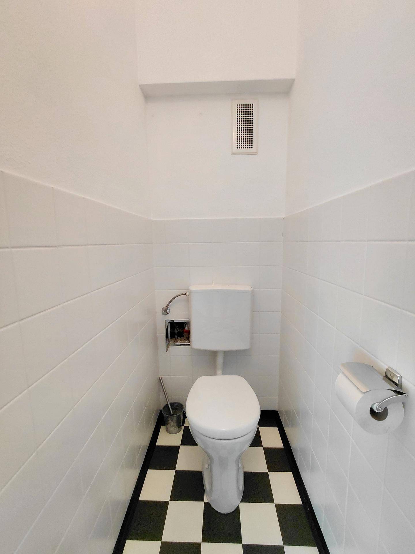Kleines WC mit weißen Fliesen, Toilette und schwarz-weiß kariertem Boden.