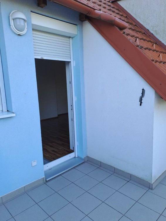 Kleiner Balkon mit grauen Fliesen und Zugang zu einem Zimmer, umgeben von einem Ziegeldach.