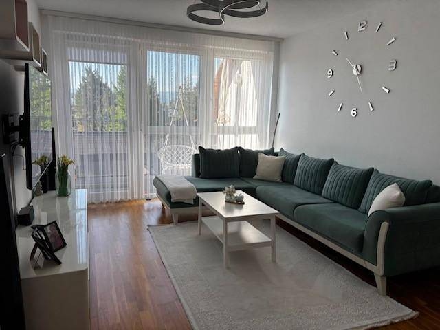 Geräumiges Wohnzimmer mit großem grünen Sofa, Holzboden und Zugang zu einem Balkon.