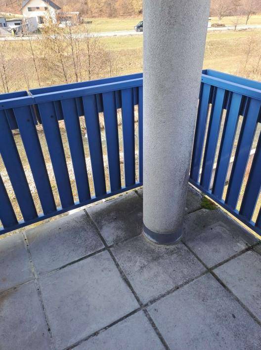 Balkon mit blauen Geländern und grauen Fliesen, bietet einen weiten Blick ins Grüne.