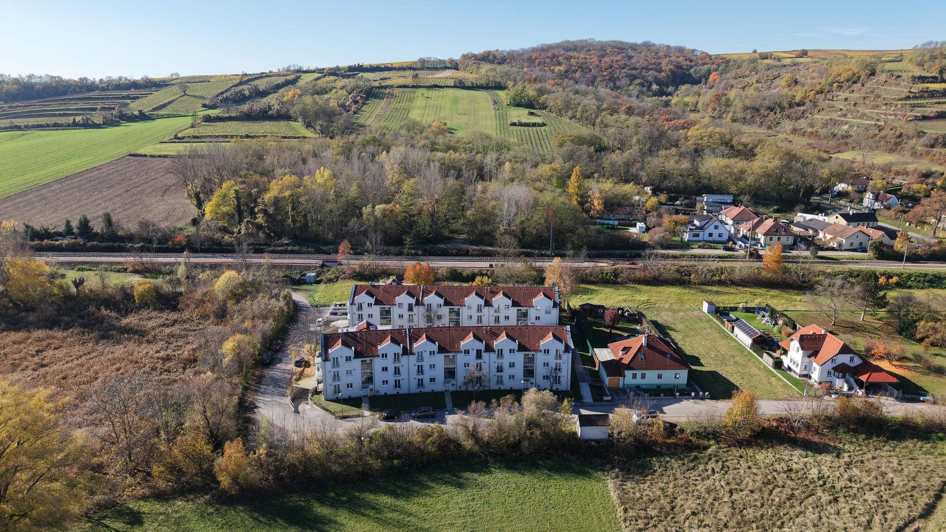 Luftaufnahme eines Wohnkomplexes umgeben von Feldern und Weinbergen in ländlicher Umgebung.