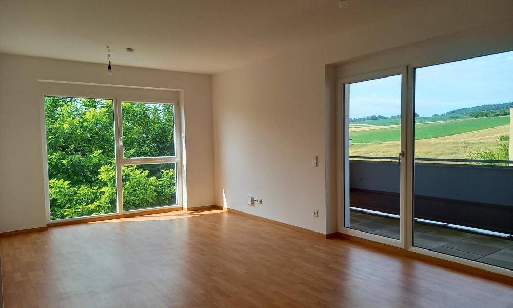 Helles Wohnzimmer mit Holzboden, großen Fenstern und Zugang zu einem Balkon mit Weitblick.