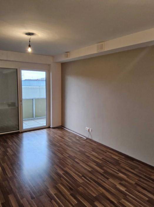 Helles Zimmer mit Laminatboden, beigen Wänden und großem Schiebetürzugang zum Balkon.