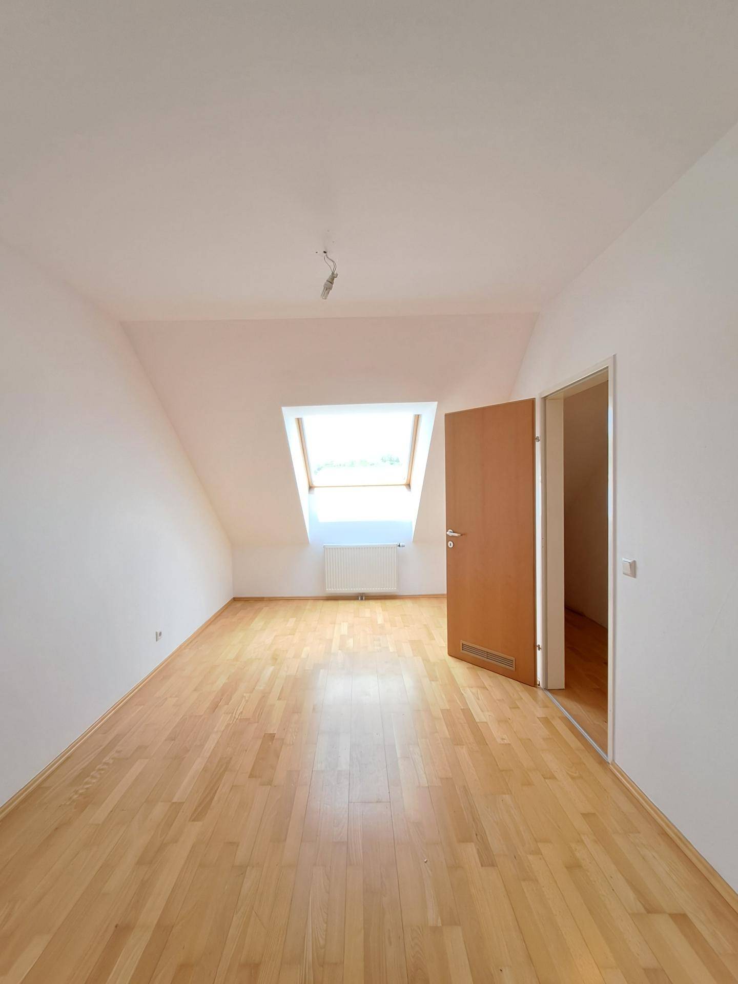 Helles Zimmer im Dachgeschoss mit Holzboden, Dachfenster und schrägen Wänden.