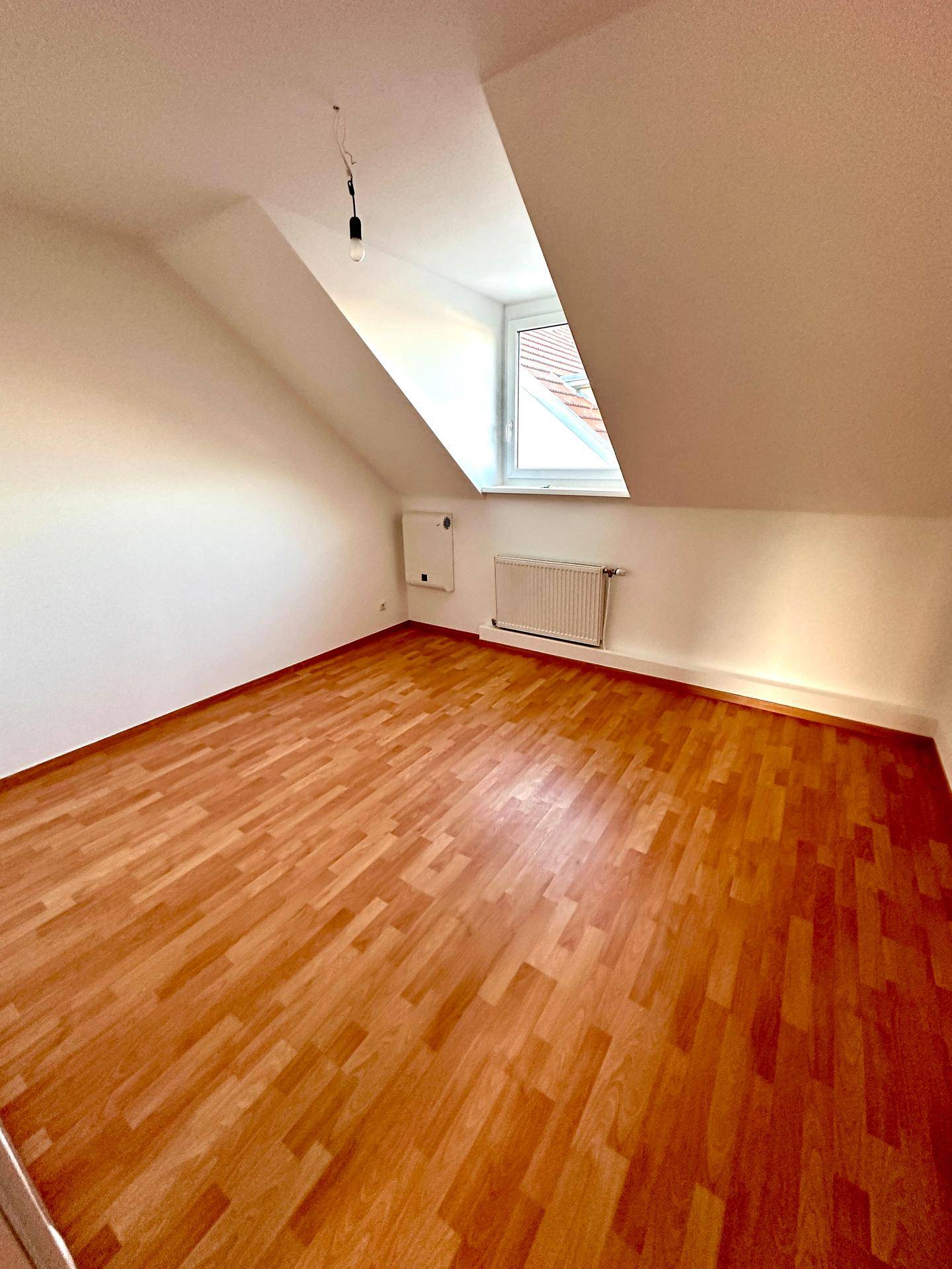 Geräumiges Schlafzimmer mit Laminatboden, Dachschräge und Fenster, gut beleuchtet.