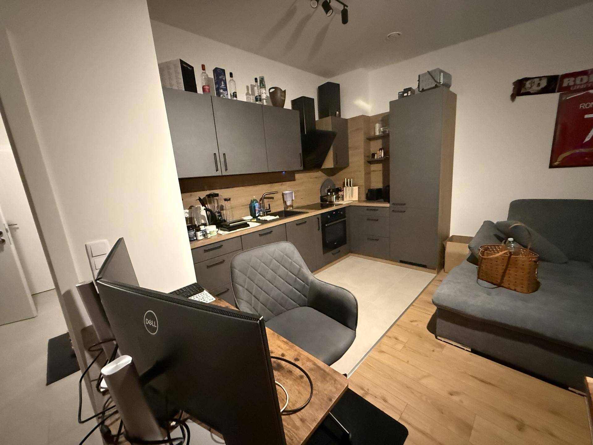 Moderne Küche mit grauen Schränken, Holzarbeitsplatte und integriertem Arbeitsplatz im offenen Wohnbereich.