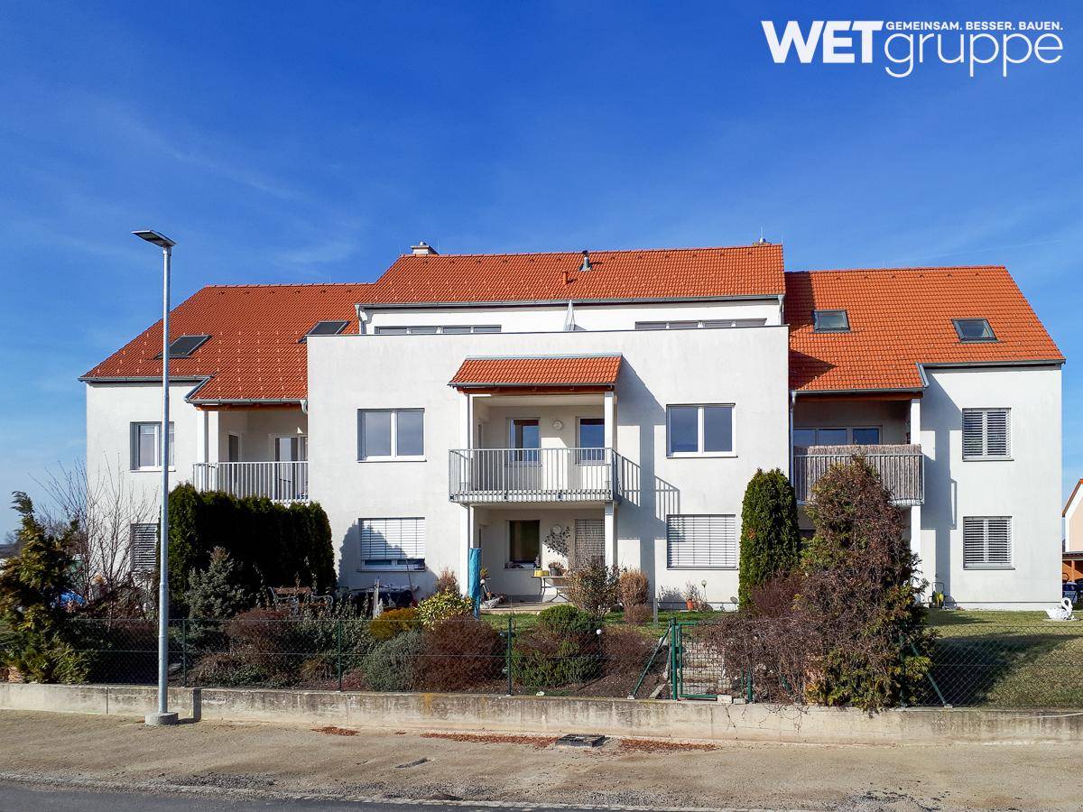 Modernes Mehrfamilienhaus mit weißer Fassade, roten Ziegeldächern und Balkonen.
