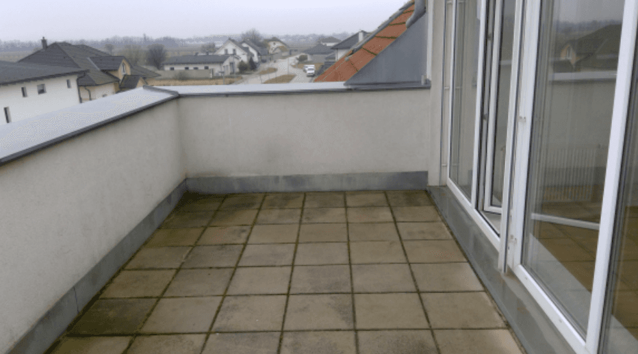 Geräumige geflieste Terrasse mit großen Fenstertüren und Blick auf die umliegende Wohnsiedlung.