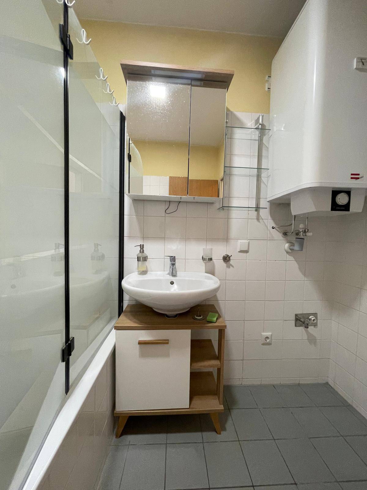 Badezimmer mit Badewanne, Waschbecken, Spiegelschrank und Warmwasserboiler.