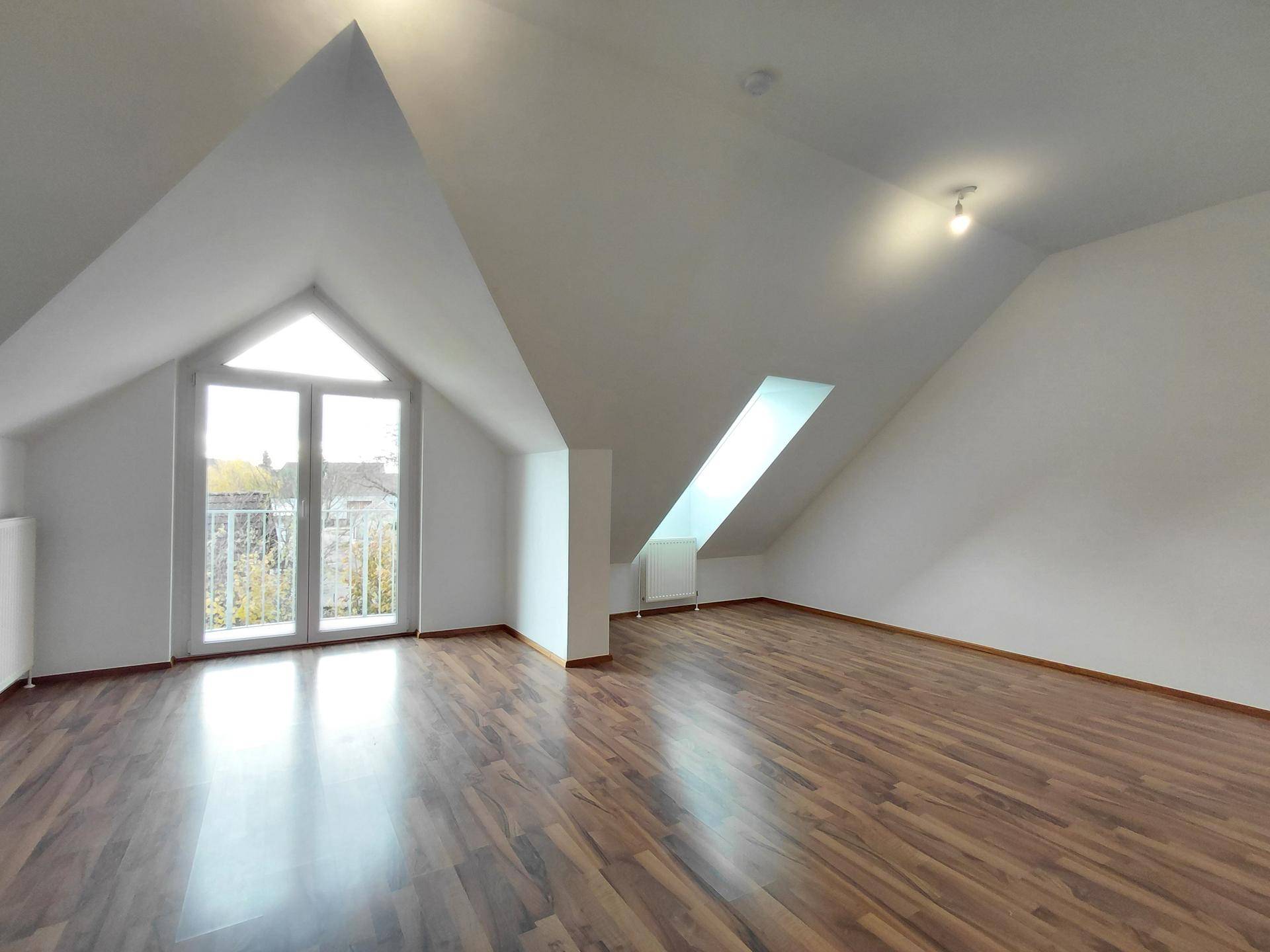 Heller Wohnbereich im Dachgeschoss mit Schrägdecke, Zugang zum Balkon und einem Dachfenster.