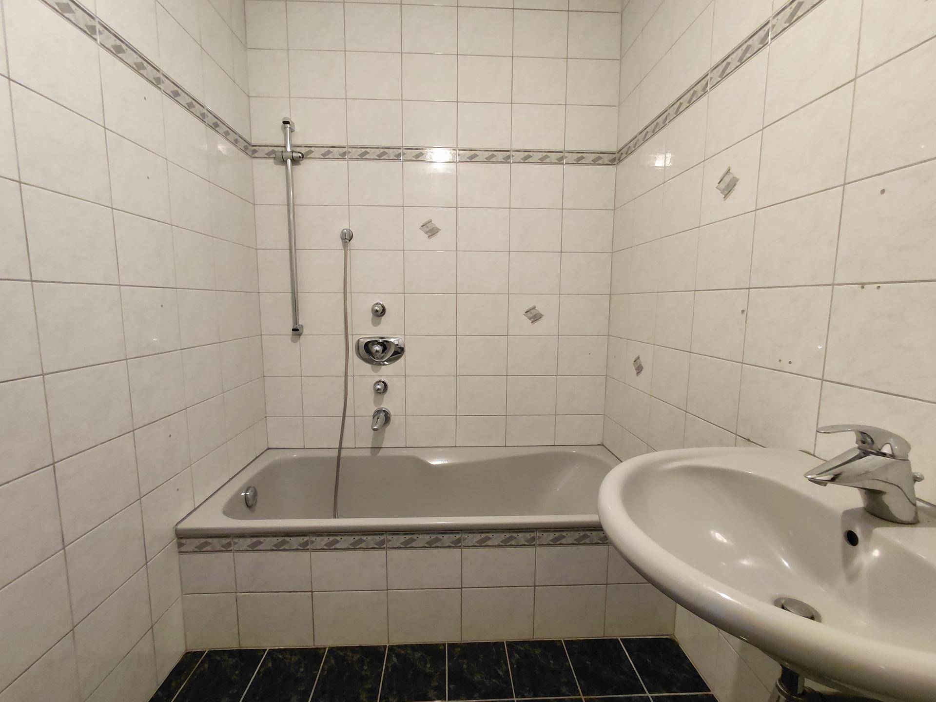 Badezimmer mit Badewanne, Waschbecken und weißen Fliesen, typisch für die 80er Jahre.