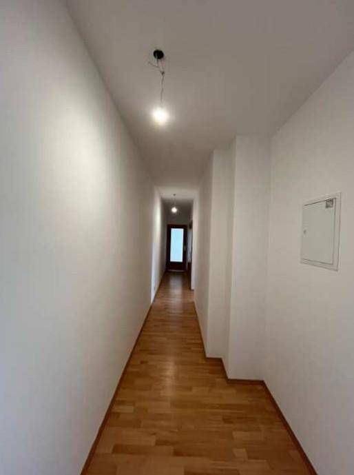 Langer, heller Flur mit Holzparkettboden und weißen Wänden, der zu weiteren Räumen führt.