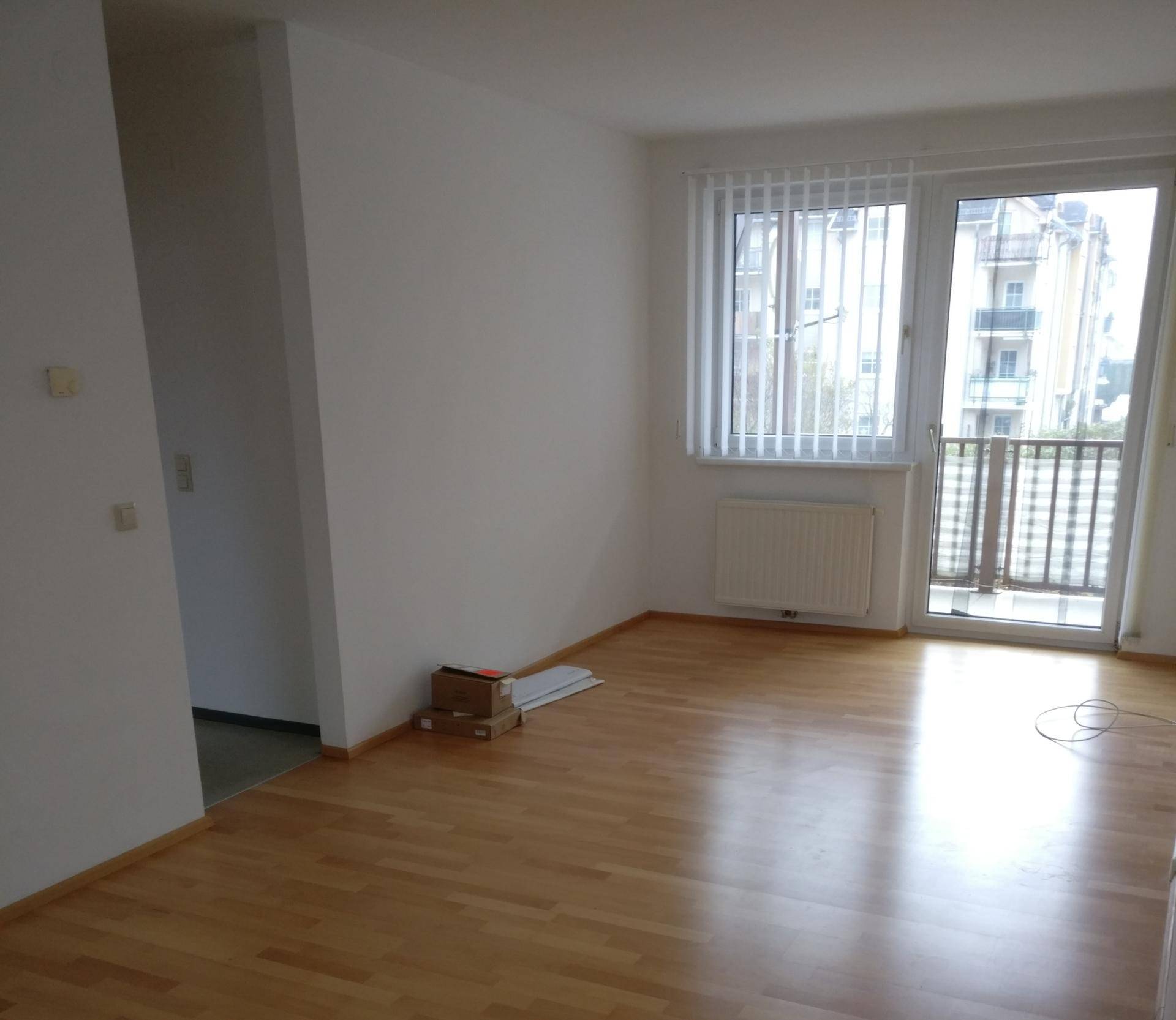 Helles, leeres Wohnzimmer mit Holzboden und Zugang zu einem französischen Balkon.
