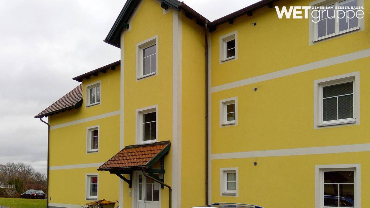 Gut erhaltenes Wohnhaus mit leuchtend gelber Fassade, weißen Fensterrahmen und traditionellem Ziegeldach.