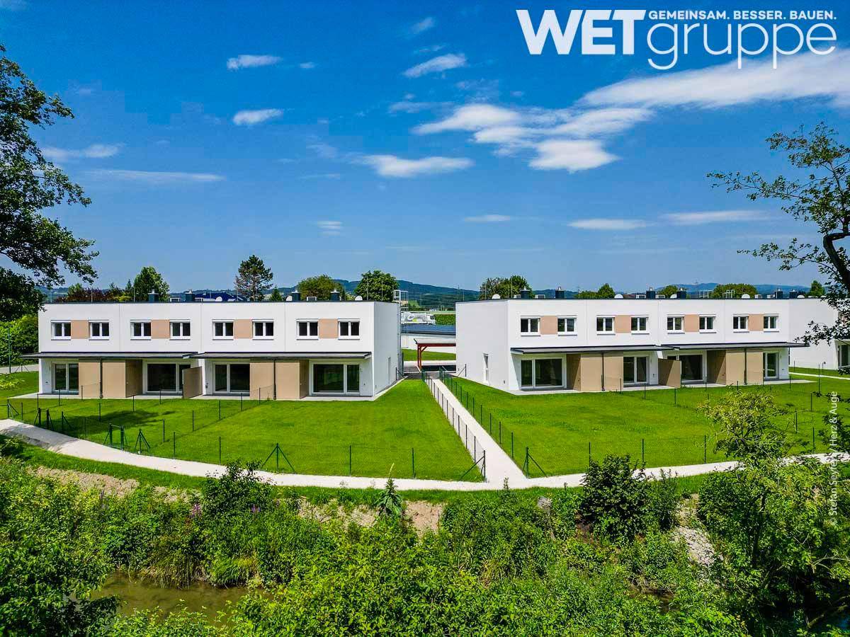Moderne Reihenhäuser mit großen Rasenflächen und Blick auf die Landschaft unter blauem Himmel.