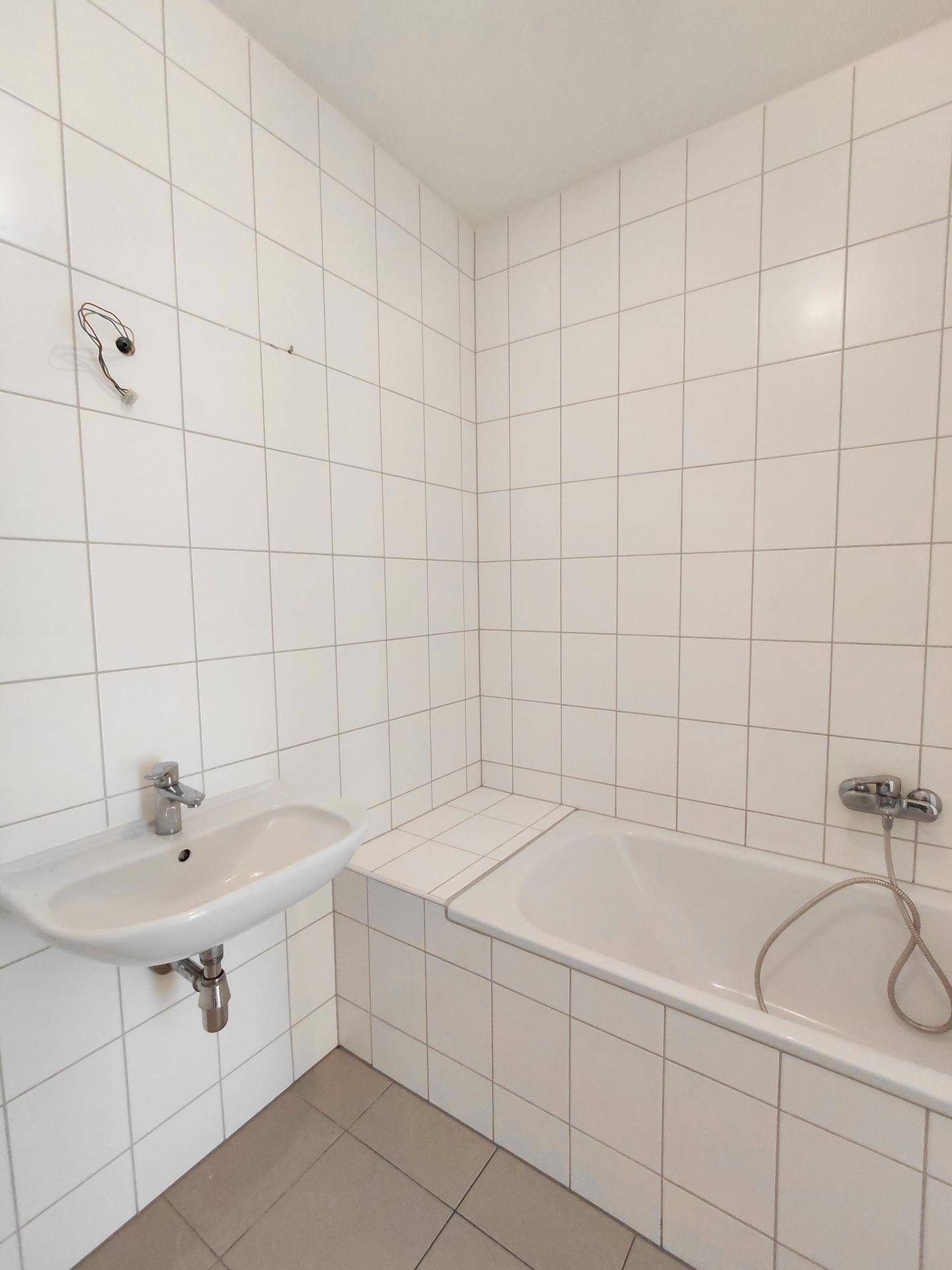 Badezimmer mit Badewanne und Waschbecken, komplett gefliest in hellem Design, praktisch und pflegeleicht.