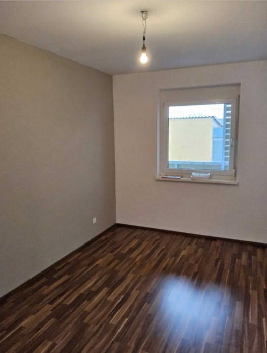 Leeres Zimmer mit Laminatboden, hellbeigen Wänden und einem Fenster für Tageslicht.