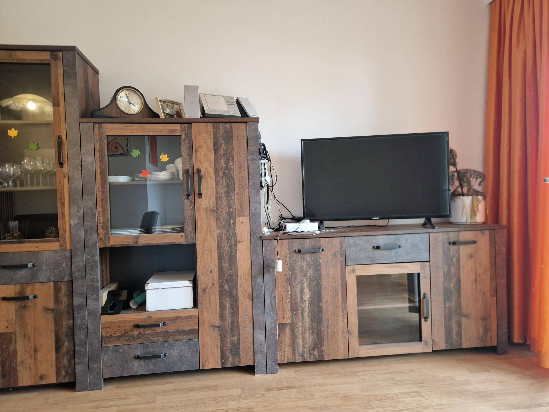 Wohnzimmer mit rustikalen Holzmöbeln, einem Fernsehschrank und Vitrinen für Geschirr.