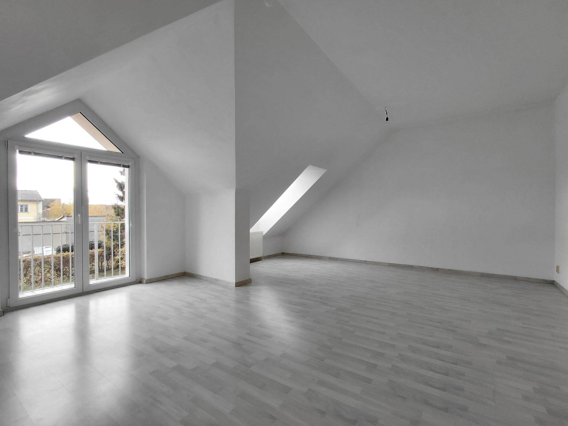 Geräumiger Wohnbereich im Dachgeschoss mit hellem Laminatboden und Zugang zum Balkon.
