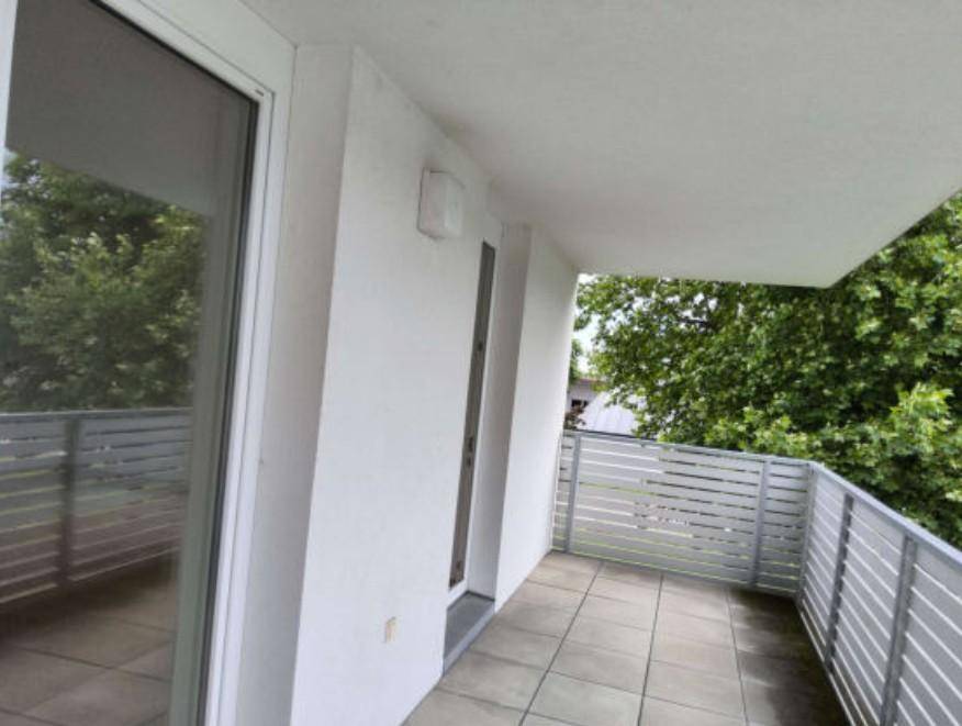 Geräumiger Balkon mit Fliesenboden und Metallgeländer, umgeben von grünen Bäumen.