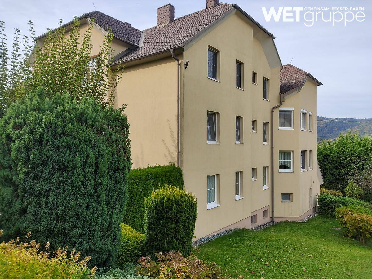 Seitenansicht des Gebäudes mit gelber Fassade, braunem Dach und gepflegtem Gartenbereich.