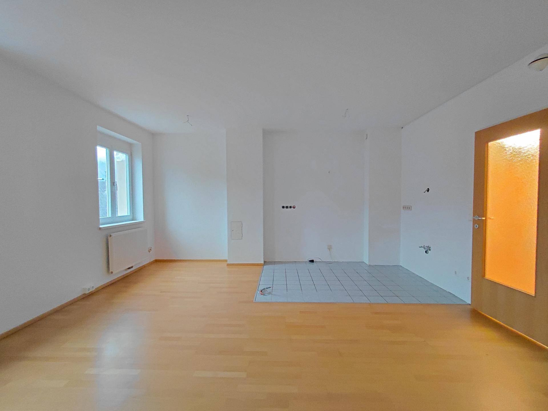Geräumiger Wohnbereich mit Parkettboden und einem gefliesten Bereich für eine zukünftige Küche.