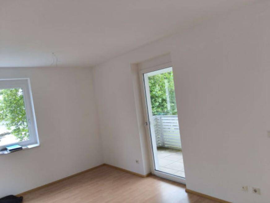 Helles Zimmer mit Holzboden, weißen Wänden und Zugang zu einem Balkon mit Blick ins Grüne.