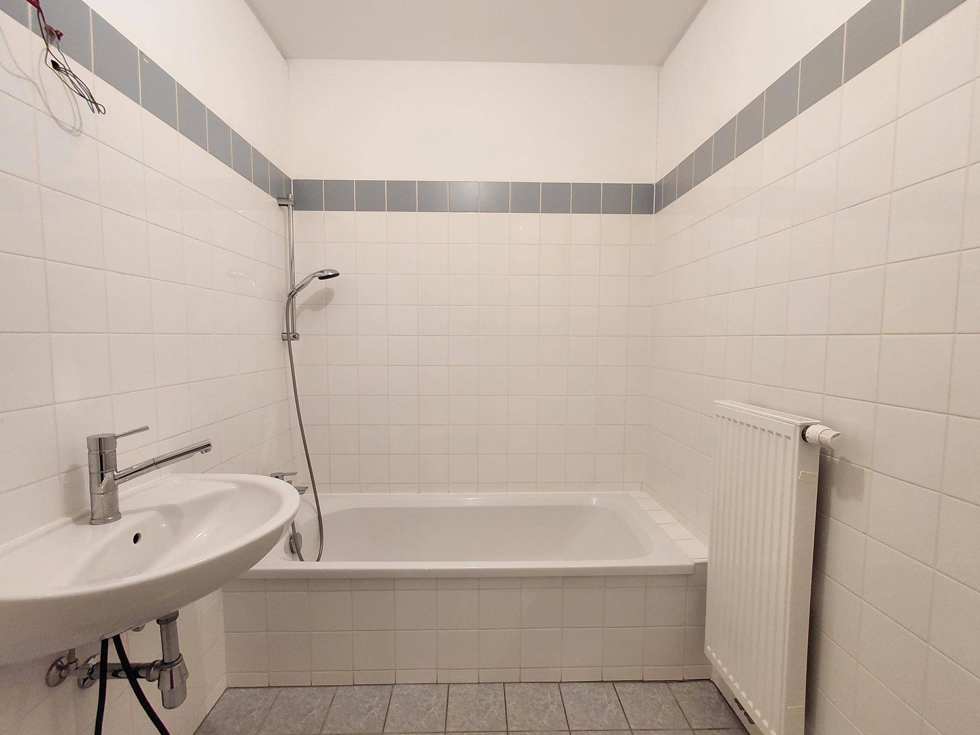 Badezimmer mit Badewanne, Waschbecken und weißen Fliesen, in einem gepflegten Zustand.