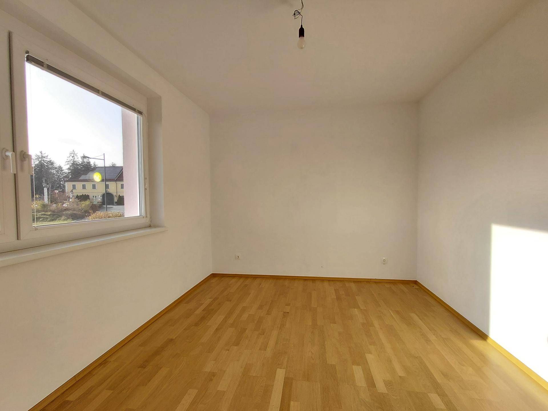 Helles Zimmer mit Holzboden und Blick auf die Umgebung, bereit zur individuellen Gestaltung.