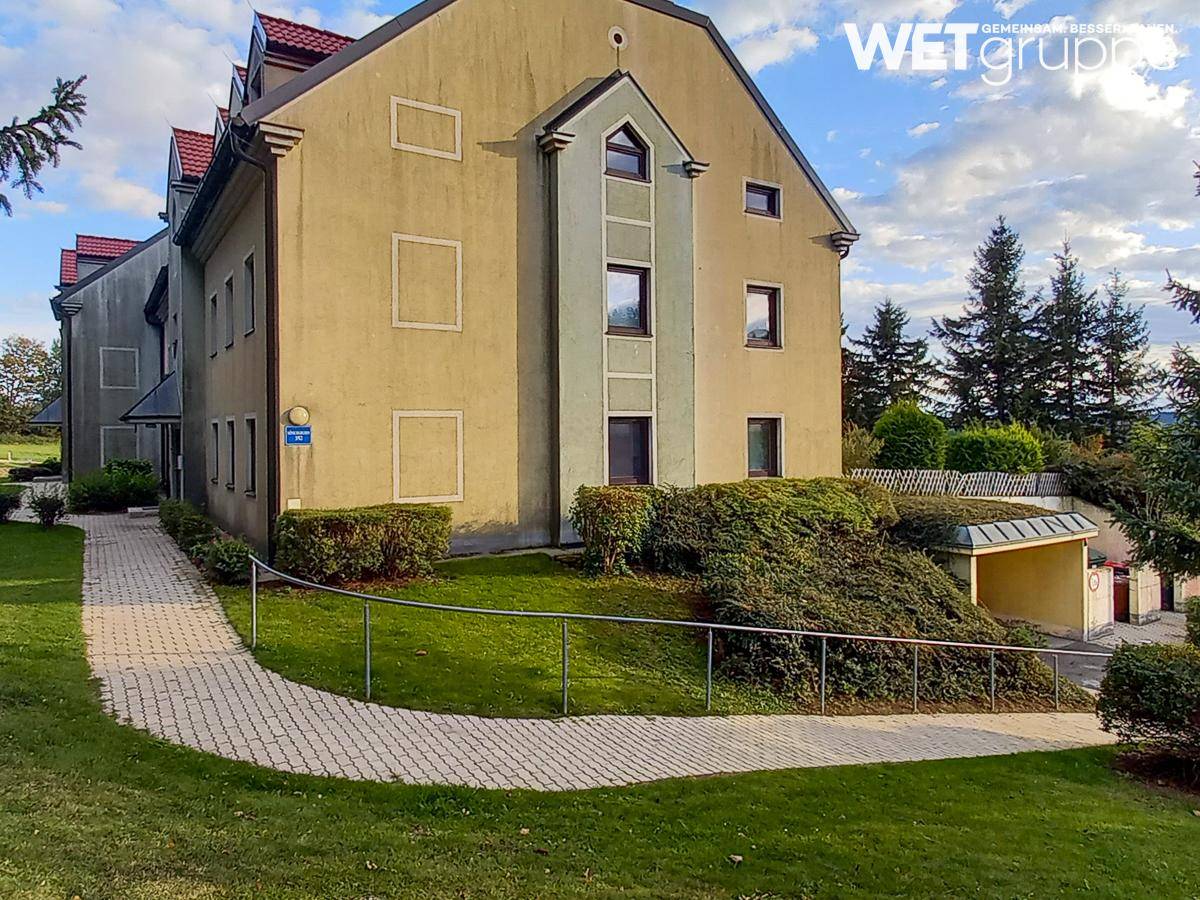 Gepflegtes Mehrfamilienhaus mit gelber Fassade, umgeben von Grünflächen und einem geschwungenen Gehweg.
