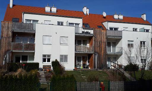 Modernes Mehrfamilienhaus mit weißer Fassade, roten Ziegeldächern und mehreren Balkonen, umgeben von einem gepflegten Garten.