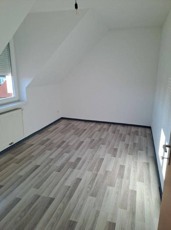 Helles Dachzimmer mit schrägen Wänden, Laminatboden und einem Fenster mit Rollladen.
