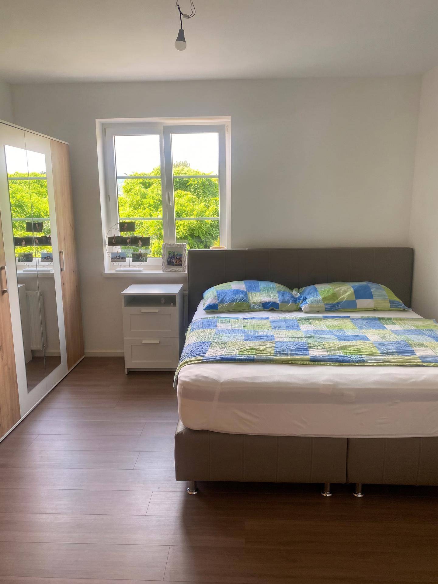 Schlafzimmer mit Doppelbett, Spiegelschrank und einem Fenster mit Blick ins Grüne.